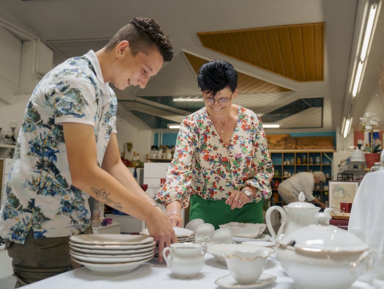 eine Frau und ein Mann stellen Geschier auf einen Tisch weil diese zum verkauf gedacht sind 