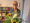 Eine lächelnde Frau mit Brille hält einen großen Blumenstrauß mit Sonnenblumen und weißen Rosen. Im Hintergrund befindet sich ein Büroregal mit bunten Ordnern.
