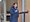 Eine lächelnde Frau mit Brille steht in einer blauen Jacke vor einem Rednerpult und hält ein Mikrofon in der Hand. Sie scheint gerade eine Rede zu halten.